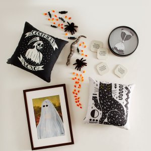 Image of halloween themed framed artwork, throw pillow, clock and bag, lying on a white surface.