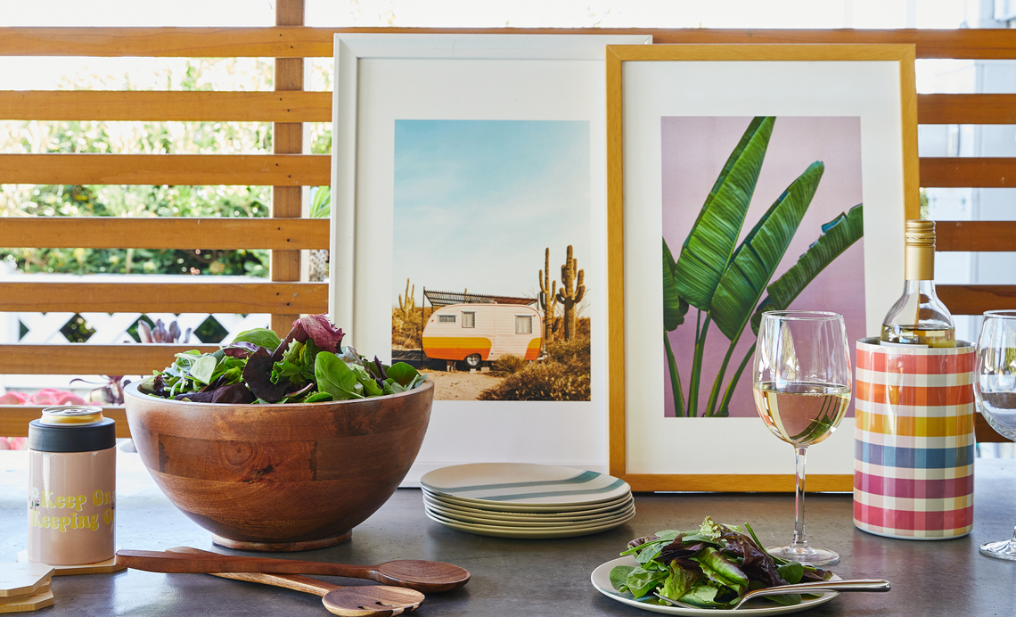 Table set with bowl of salad, plates, and glassware, featuring framed artwork leaning against the wall