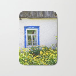 Old rustic house with high yellow flowers in the garden Bath Mat