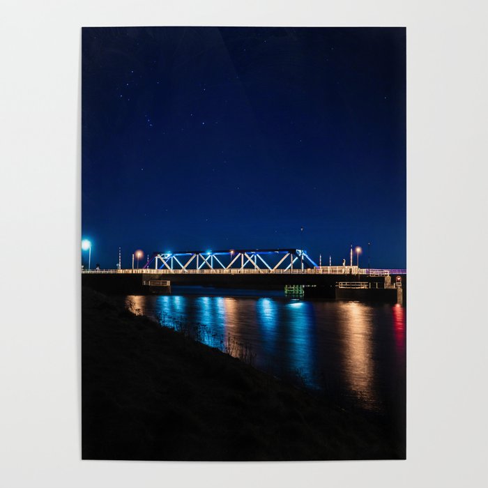 Bridge illuminated by street lights which are reflected by the water. Poster
