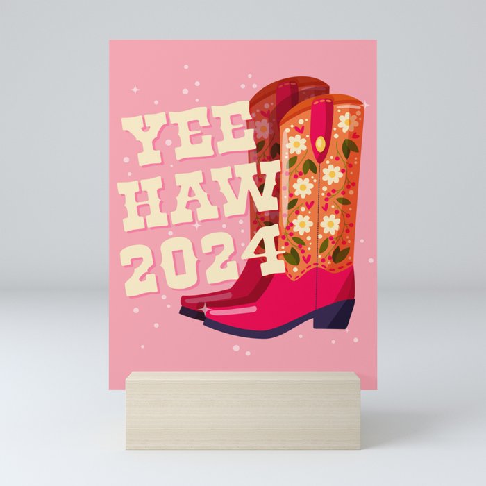 A pair of cowboy boots decorated with flowers and a hand lettering message Yeehaw 2024 on pink background. Happy New Year colorful hand drawn vector illustration in bright vibrant colors. Mini Art Print