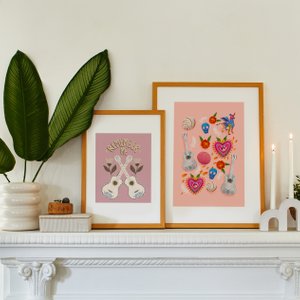 Image of two framed coco art pieces on top of mantle with candles and plant