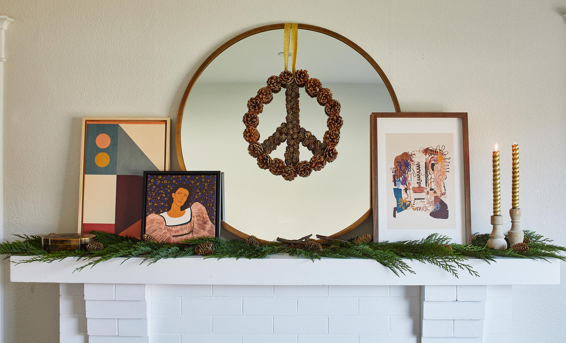 framed prints on a mantel, next to a pinecone wreath in the shape of a peace sign