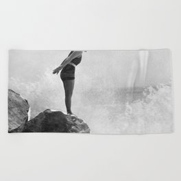 Female swimmer on rock above crashing surf Beach Towel