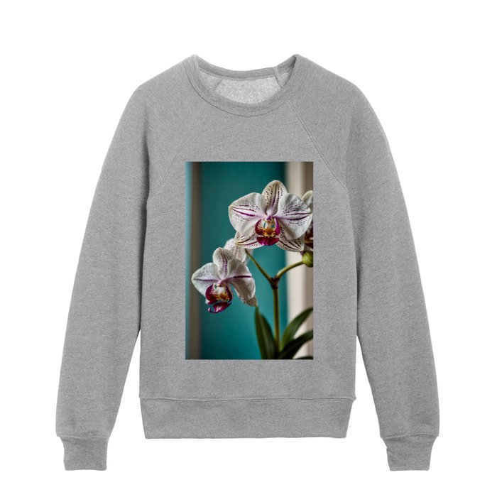 An orchid with white flowers on a turquoise background illuminated by the light of a side window Kids Crewneck