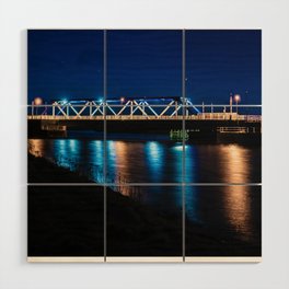Bridge illuminated by street lights which are reflected by the water. Wood Wall Art