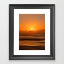 Birds flying across a sunset at the beach Framed Art Print