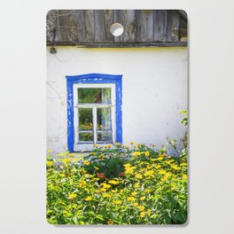 Old rustic house with high yellow flowers in the garden Cutting Board