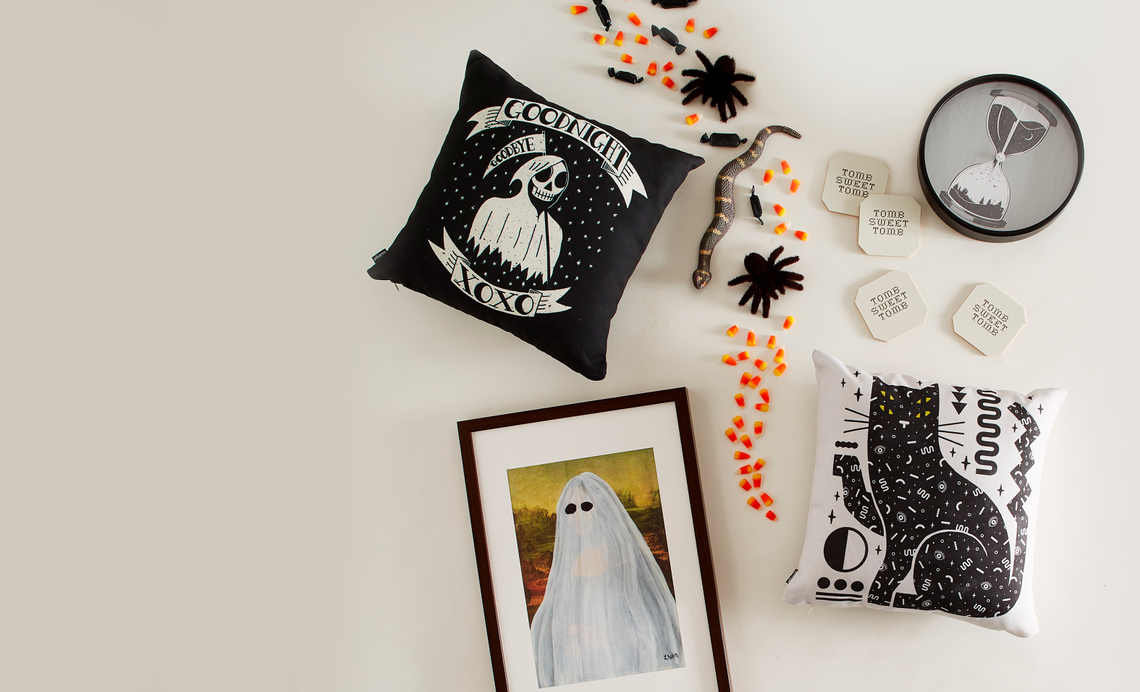 Image of halloween themed throw pillow, framed art and clock on a white table with halloween candy around.