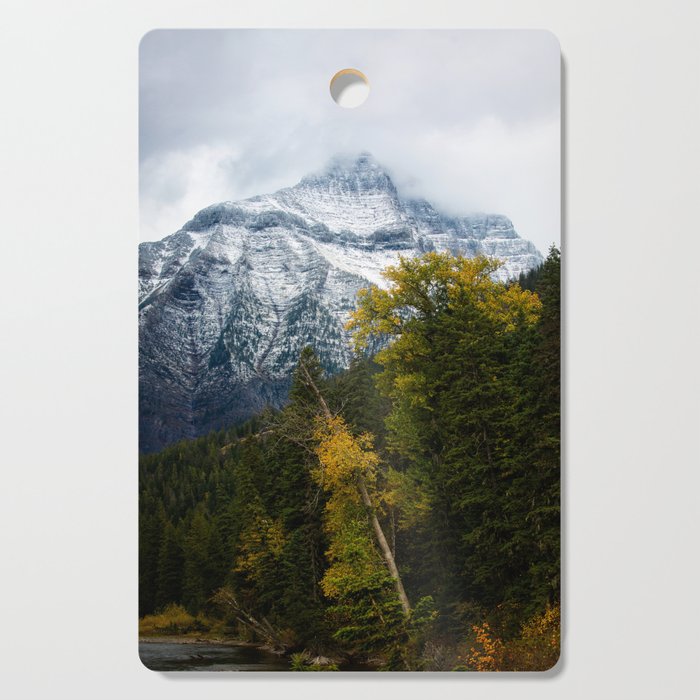 Transitions - Snowy Mountain Peak Overlooking Trees with Fall Color on Autumn Day in Glacier National Park Montana Cutting Board