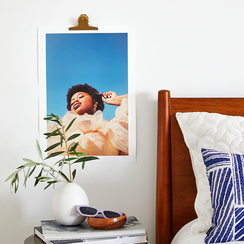 art print of a woman posing in a dress, hung next to a bed